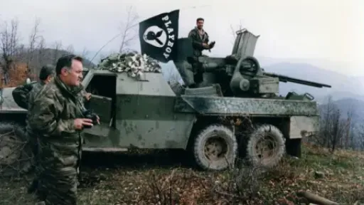 Gamma-Rapho Images via Getty Images General Mladić leads his troops in 1994. He is standing next to a military vehicle and he is holding binoculars 